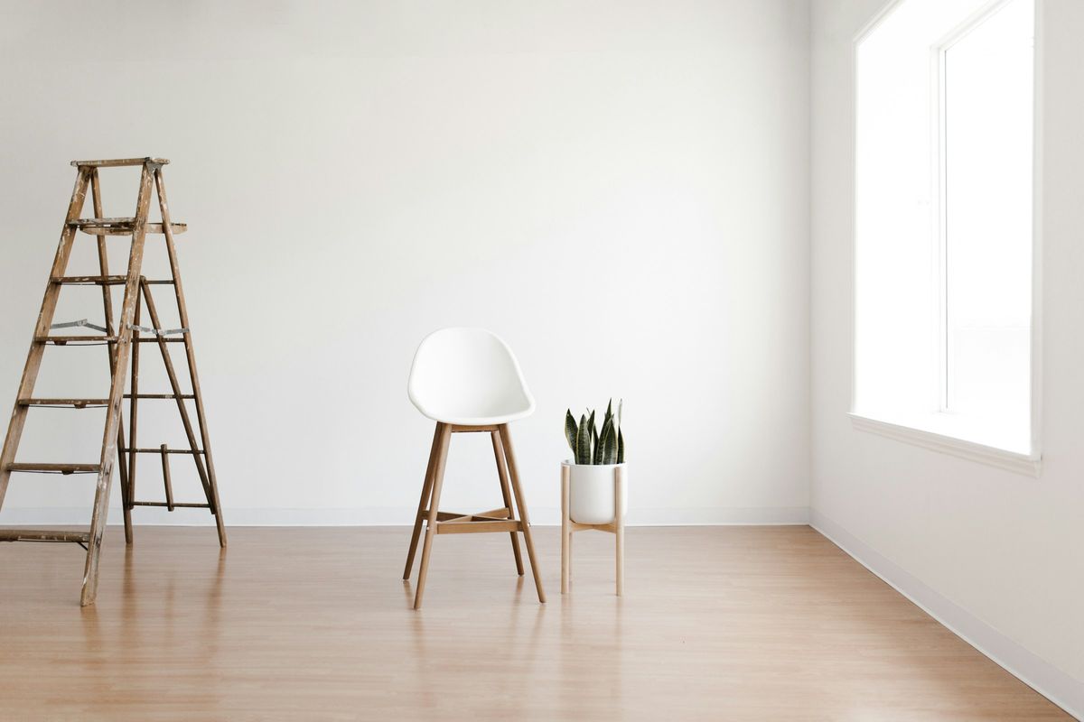 Een lege, propere kamer met een houten vloer, een ladder, een kruk en een plant