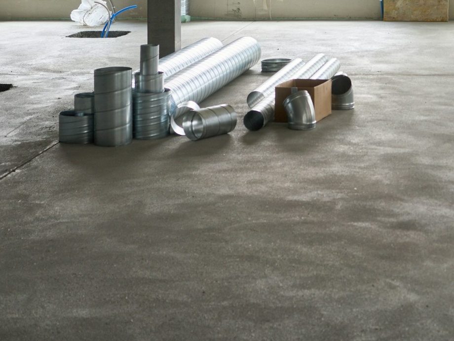 Ventilatiekanalen en bochtstukken op de betonvloer van een werf